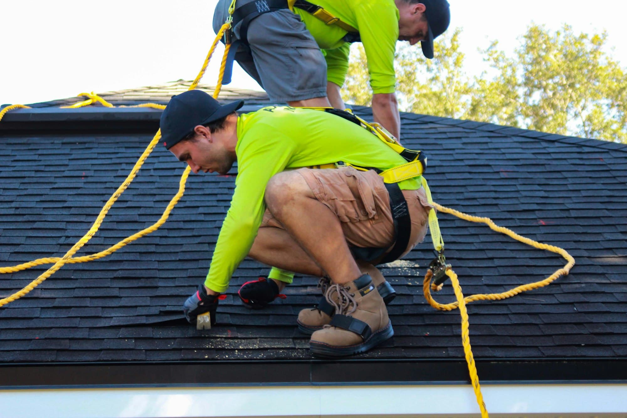 Two roofers in harnesses replacing shingles on a steep residential roof